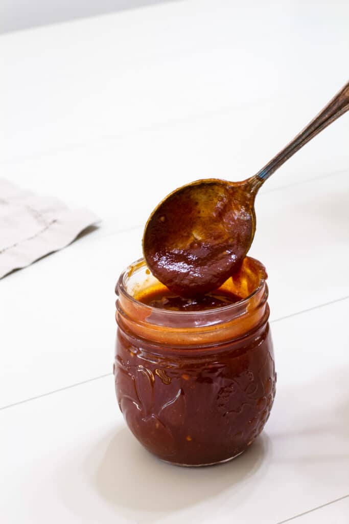 A jar of homemade chili sauce with a spoon of it above the jar.