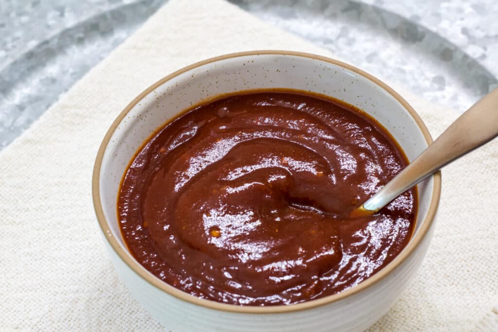 A small bowl of chili sauce and a spoon in it sitting on a cream colored cloth napkin.