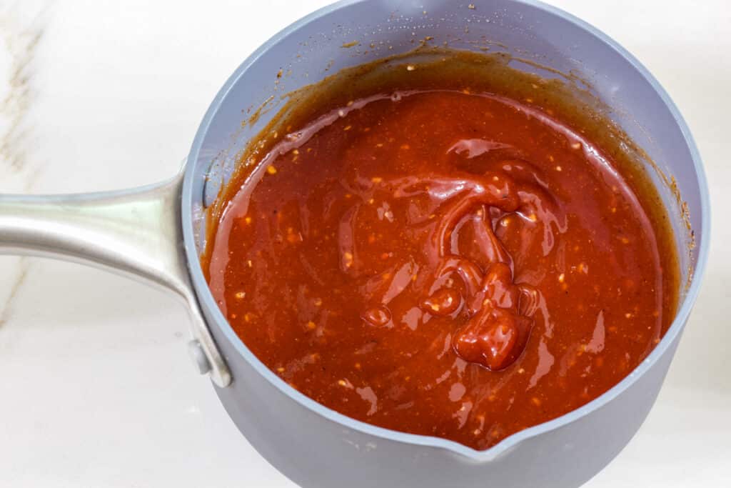 A small gray saucepan with the ingredients to make homemade chili sauce from ketchup after being mixed.