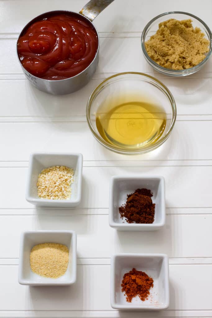 The ingredients needed to make homemade chili sauce with ketchup measured out sitting on a white table.