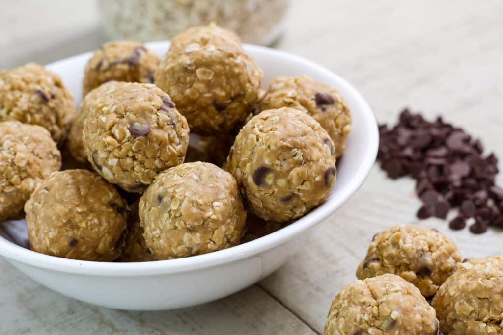 A bowl full of 4 Ingredient Protein Rich Peanut Butter Energy Balls and some chocolate chips and more energy balls sitting next to it.