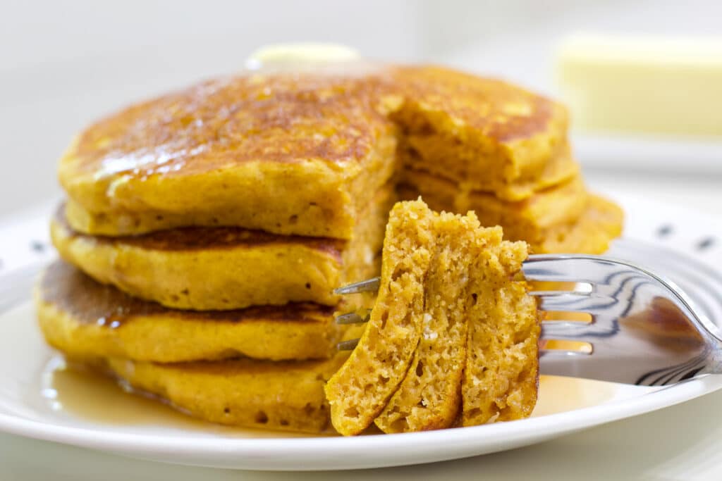 A bite of pumpkin pancakes on a fork in the foreground and the stack in the background.