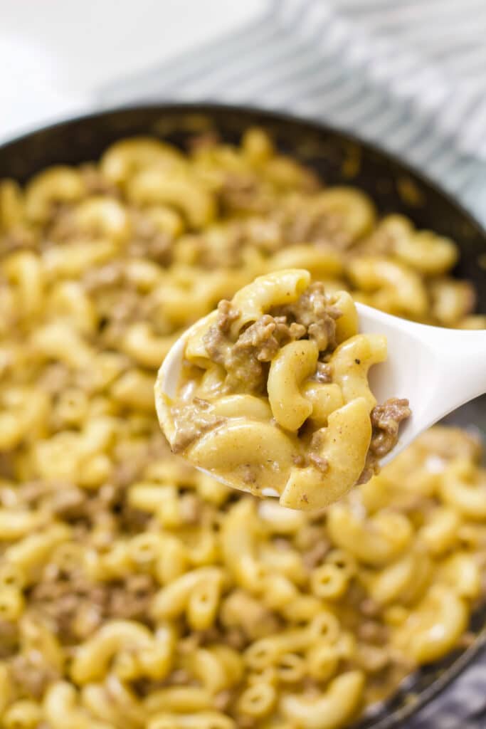A pan of cheeseburger macaroni in the background and one serving spoonful in the foreground.