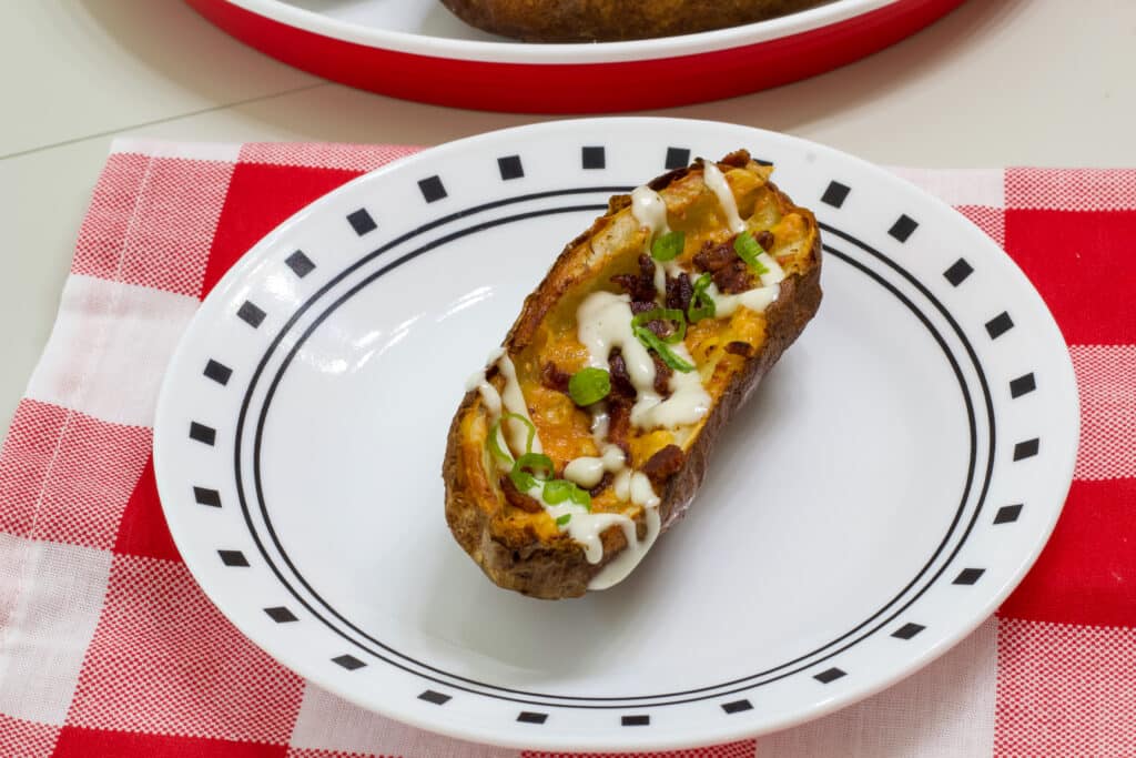 One loaded potato skin drizzled with ranch dressing on a white plate.