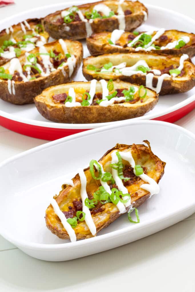 One potato skin on a white plate in the foreground and several on a plate in the background.