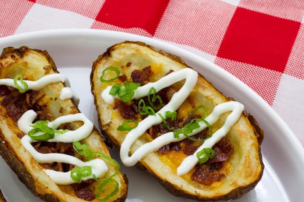 Two Homemade Loaded Potato Skins made in the Air Fryer on a white plate that is sitting on a red and white napkin.