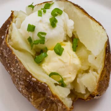 Very close up overhead angle of a baked potato topped with butter, sour cream and green onions.