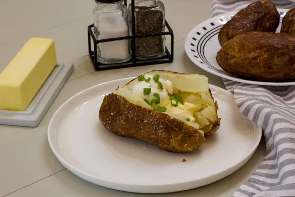 A plate with one baked potato, a dish with a stick of butter, salt and pepper shakers on a table.