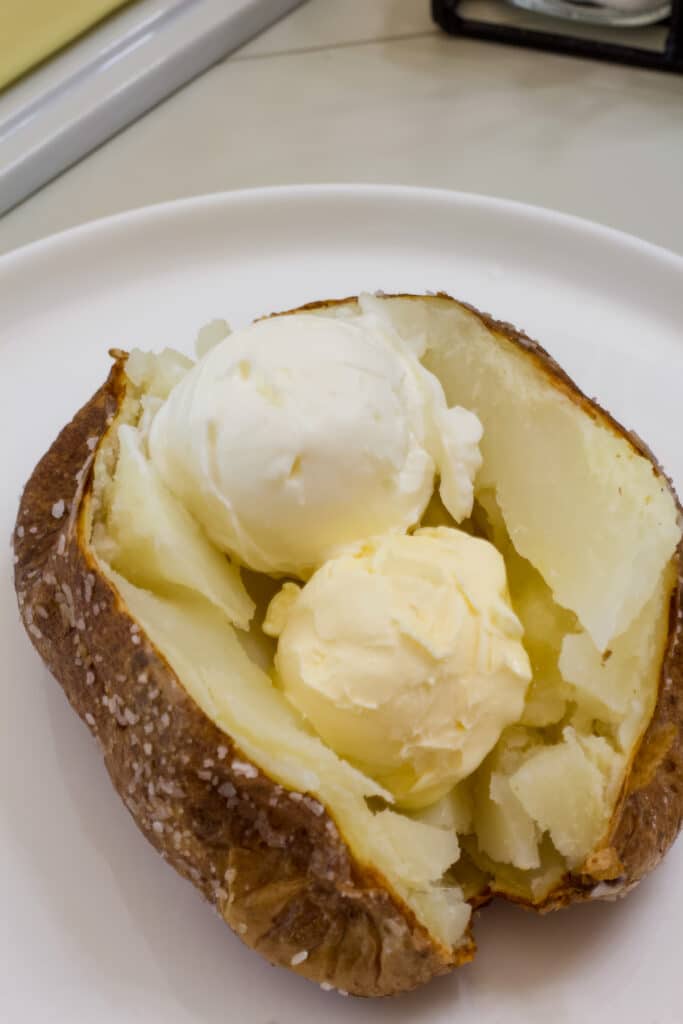 A baked potato topped with butter and sour cream on a white plate.