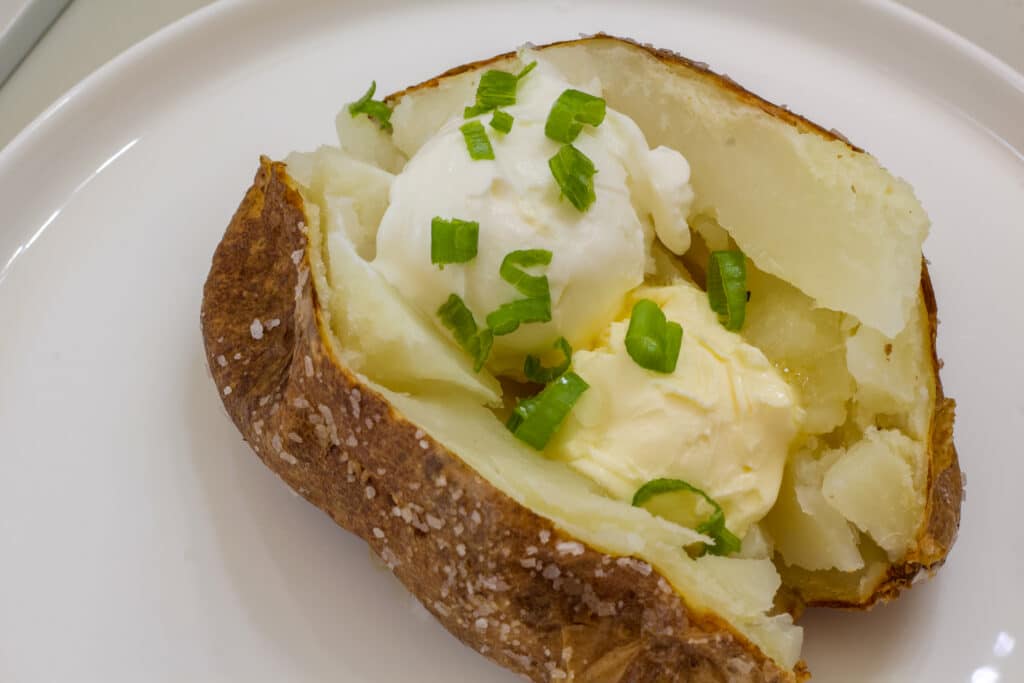 Overhead shot of a baked potato topped with butter, sour cream and green onions on a white plate.