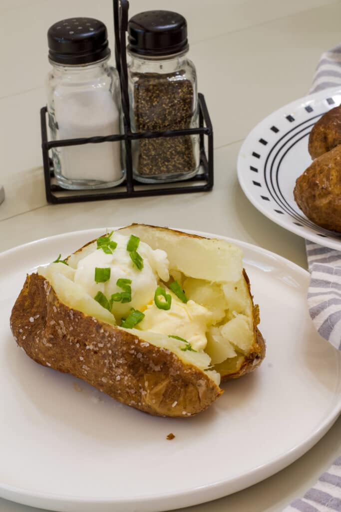 Side view of an air fryer baked potato topped with butter, sour cream and green onions.