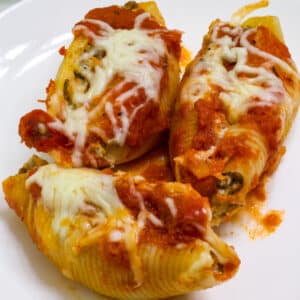 Very close up view of three stuffed pasta shells on a white plate.