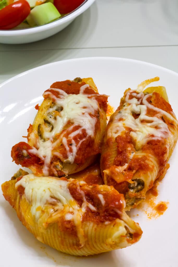 Three stuffed pasta shells on a white plate ready to eat.