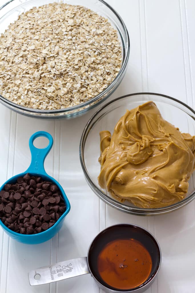 The quick oats, creamy peanut butter, pure maple syrup and chocolate chips measured out in individual bowls.