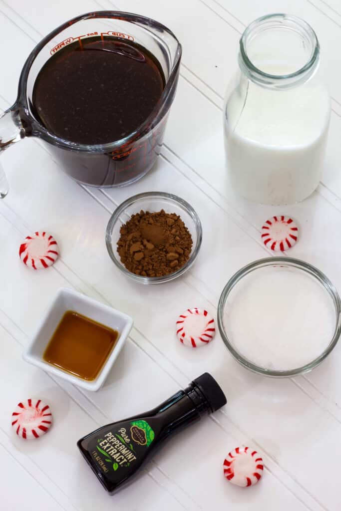 The black coffee, milk, vanilla, sugar, cocoa powder, and peppermint extract on a white table.