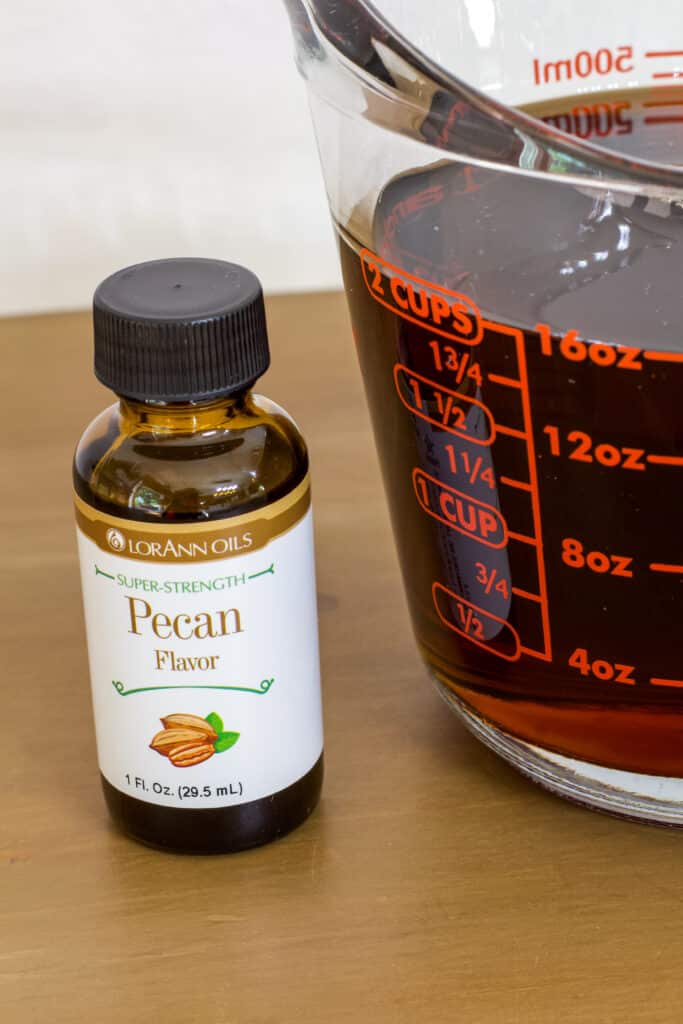 A bottle of pecan flavoring sitting next to a measuring cup with 2 cups of butter flavored pancake syrup in it.