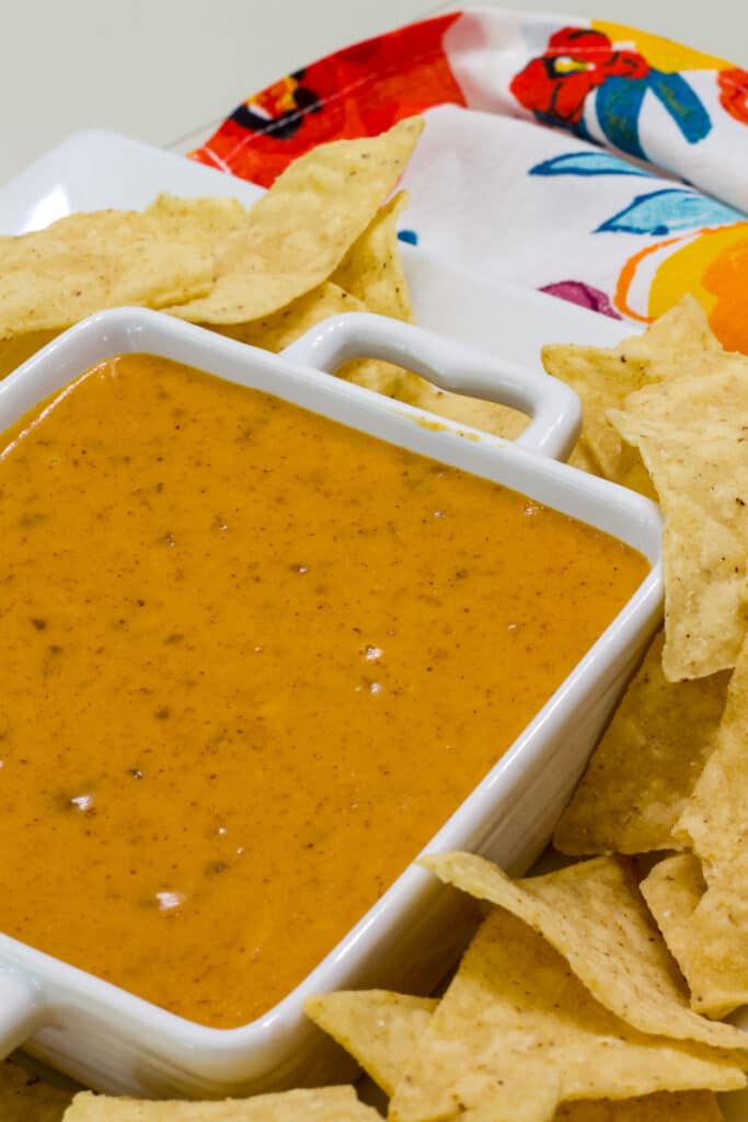 A bowl of chili cheese queso on a plate with tortilla chips.