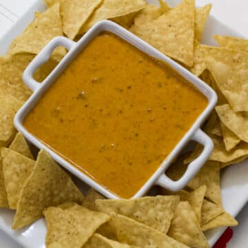 A bowl of queso surrounded by tortilla chips on a plate.