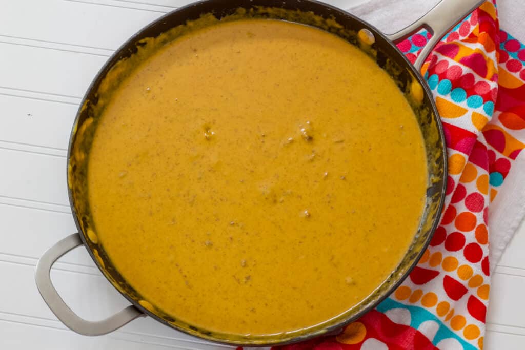 A skillet full of Copycat Chili's Skillet Queso sitting on a white table with a colorful kitchen towel next to it.
