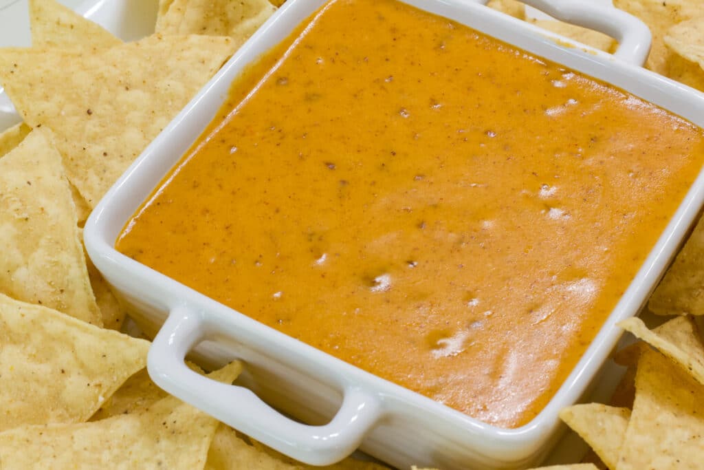 Close up of a square bowl full of chili cheese queso, it is surrounded by chips.