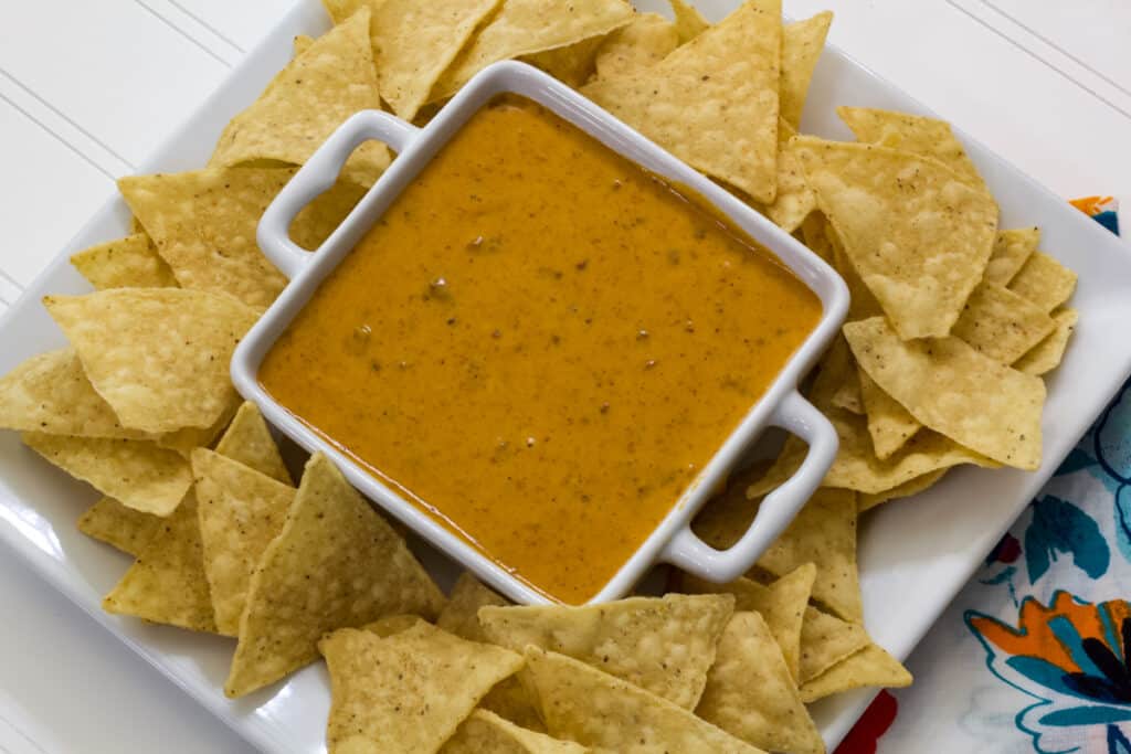 Overhead shot of a bowl of queso on a white plate with tortilla chips.
