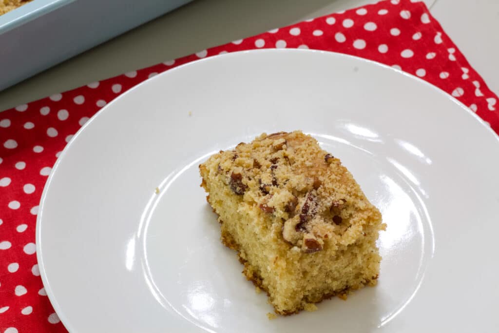 One piece of coffee cake on a white plate that is sitting on napkin that is red with white polka dots.