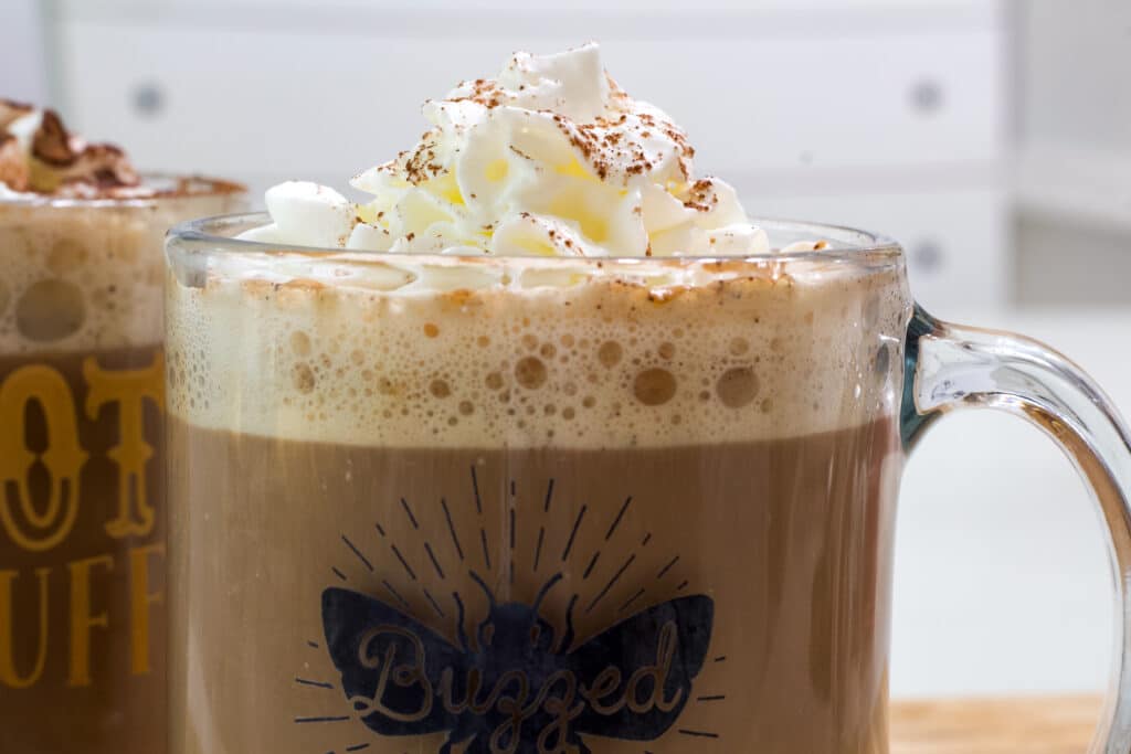 The top half of one cup of chocolate coffee is visible, it is topped with whipped cream and a dusting of cocoa powder.