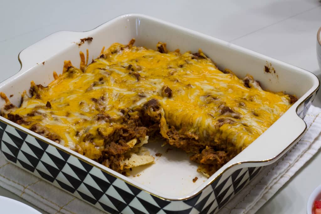 The taco salad casserole in the baking dish without toppings, one serving is missing.