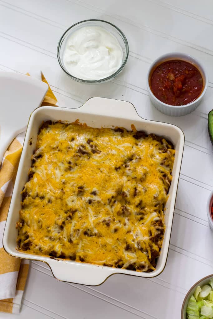 The entire baked taco salad casserole, a small bowl of sour cream anda small bowl of salsa.