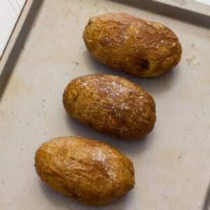 Three potatoes on a sheet pan after they have been baked in the oven without foil.