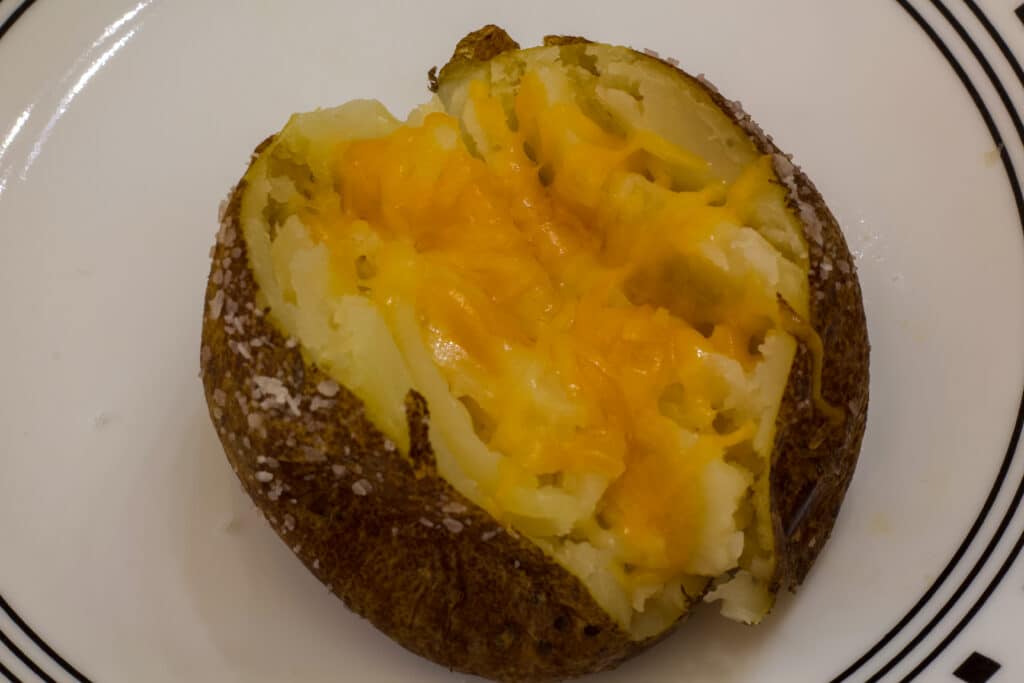 One oven baked potato topped with shredded cheese on a plate.