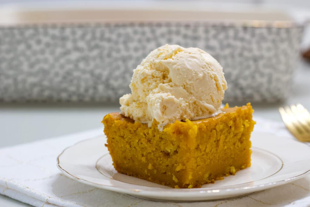 One piece of pumpkin pie cake with a scoop of vanilla ice cream on top of it.