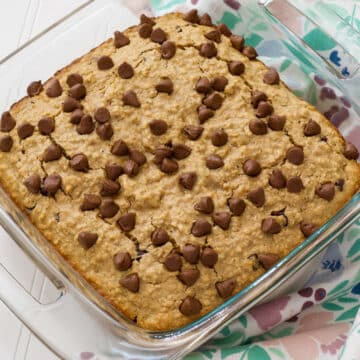 The whole Chocolate Chip Baked Oatmeal Recipe in a glass casserole dish with a floral tea towel to the right of it.