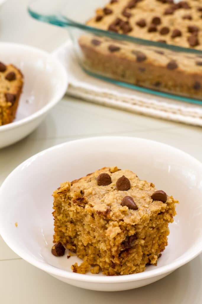 One serving of baked oats in the foreground and the casserole dish with the remaining baked oatmeal in the background.