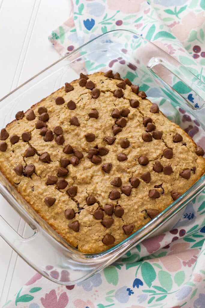 The entire Chocolate Chip Baked Oatmeal in a glass casserole dish with a floral tea towel on the right side of it.