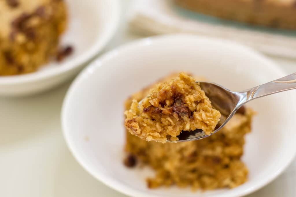 A spoonful of baked oats in the foreground and the rest of the serving in a white bowl in the background.