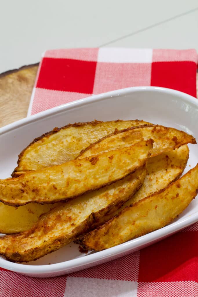 Several 20 Minute Air Fryer Potato Wedges on a white plate that is sitting on red and white checkered napkin.
