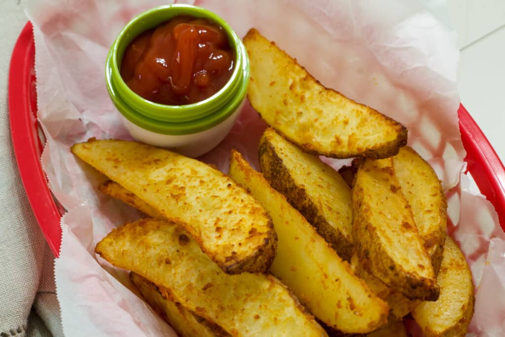 Several potato wedges in a parchment paper lined basket with a small bowl of ketchup.