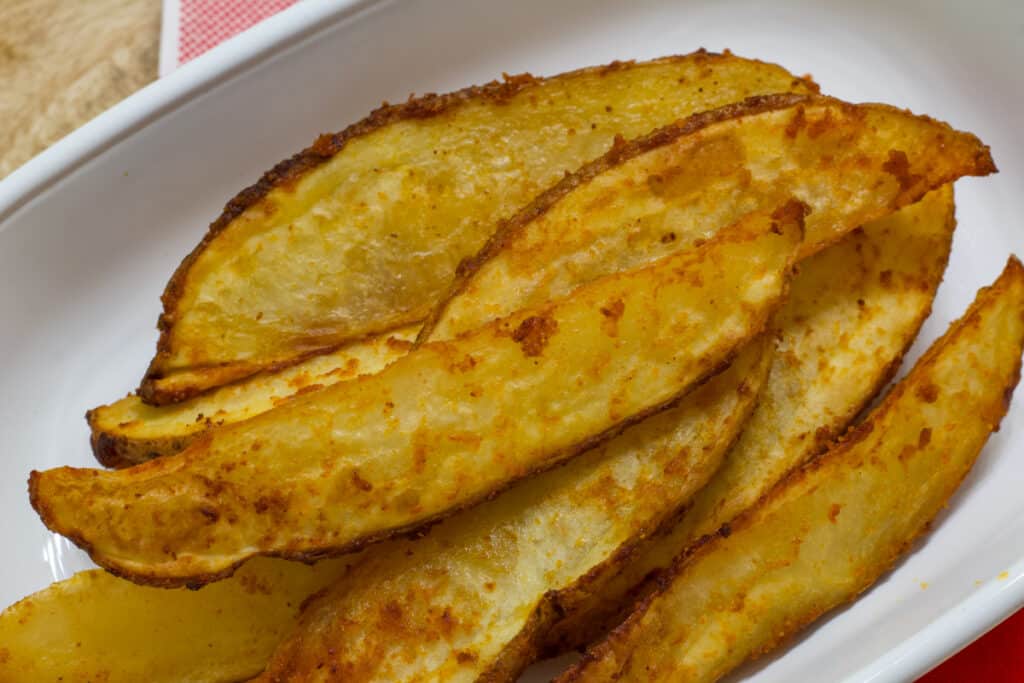 Close up overhead view of many air fried potato wedges on a white rectangular plate.