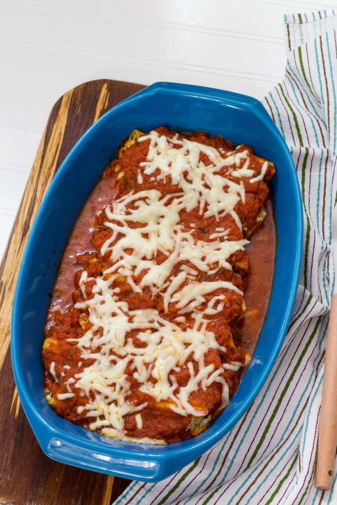 A casserole dish full of Cheese & Spinach Stuffed Manicotti with a striped tea towel next to it.