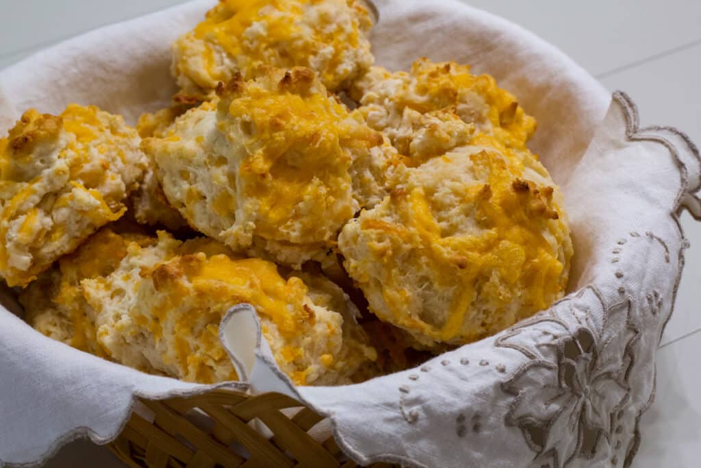 A cloth napkin lined basket full of Garlic & Cheddar Cheese Drop Biscuits ready to be served.