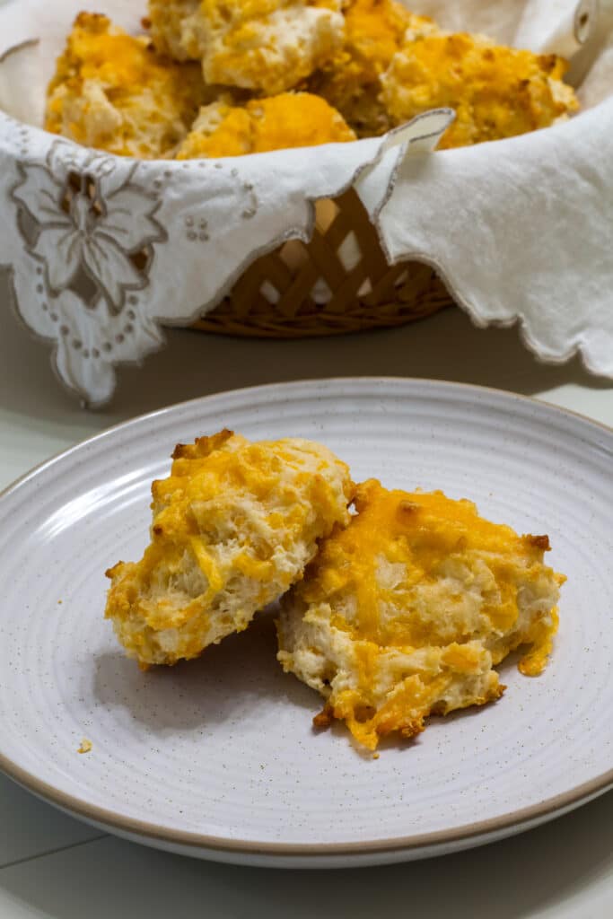 Two baked biscuits on a plate, the basket of biscuits is behind the plate.