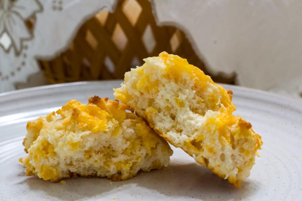 A split open baked biscuit on a plate so the fluffy inside of the biscuit is visible.