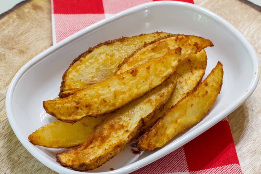 A plate with several cooked potato wedges on it.
