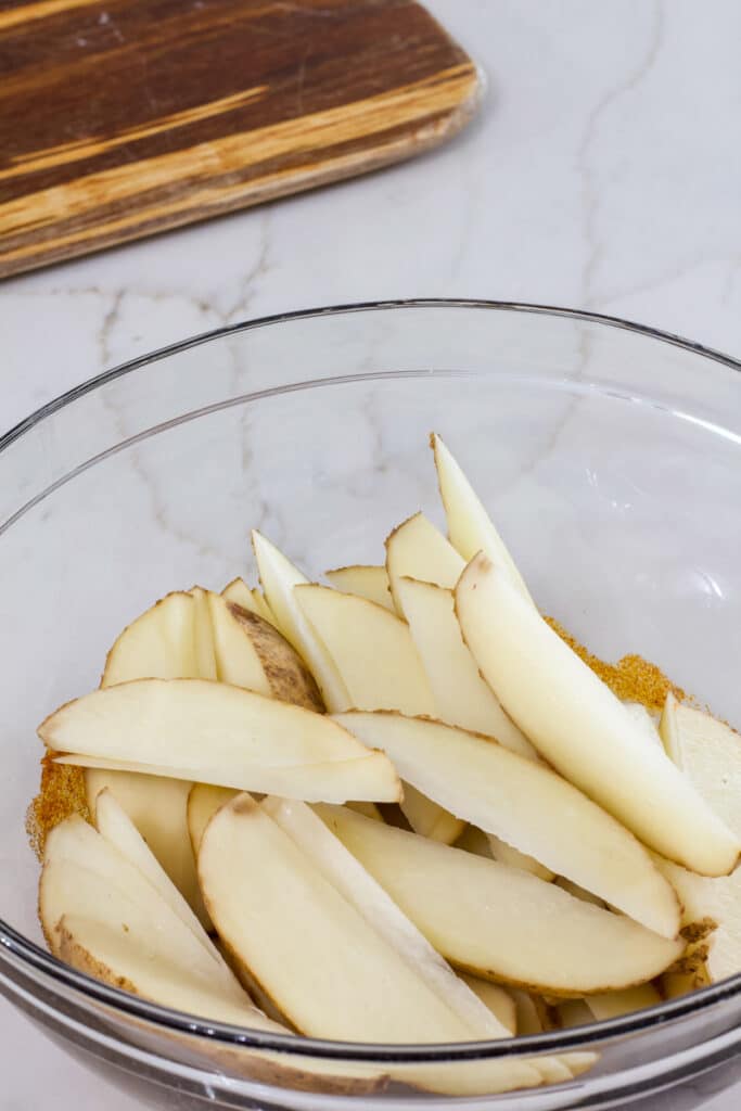 A glass bowl full of cut potato wedges.