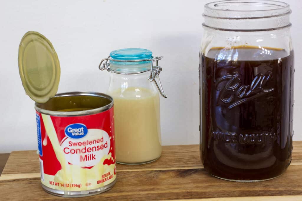A mason jar full of black coffee, a small bottle if condensed milk and the opened can of milk.