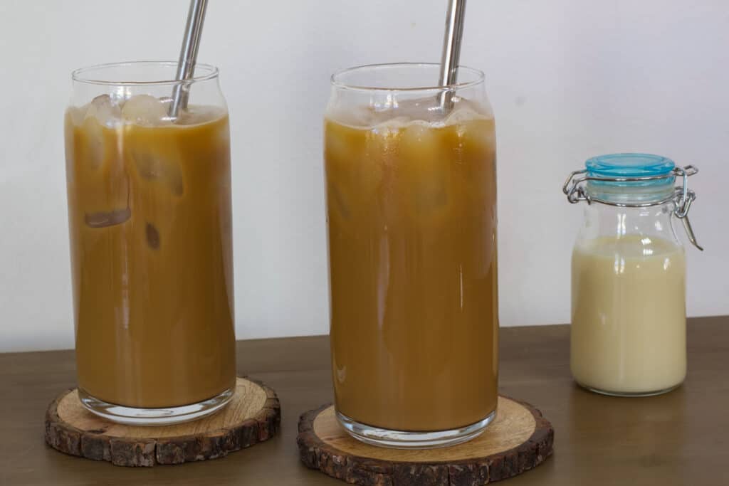 Two tall glasses of Iced Coffee Recipe with Sweetened Condensed Milk and a small bottle of condensed milk next to them.