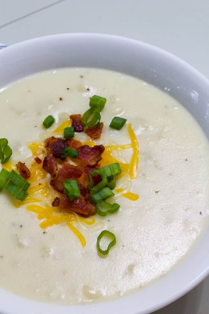 A bowl of Outback Steakhouse Potato Soup topped with bacon bits, shredded cheese and sliced green onions.