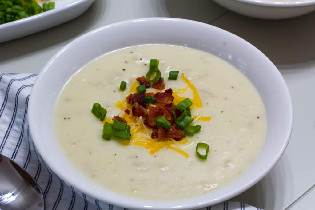 One white bowl filled with Outback Steakhouse Potato Soup and topped with cheese, scallions and chopped bacon.