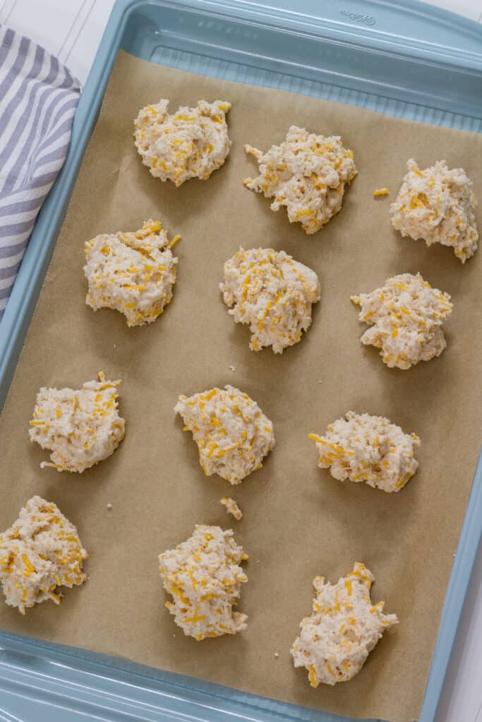 The unbaked Garlic & Cheddar Cheese Drop Biscuits on a parchment lined baking sheet ready to go into the oven.